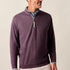 Man wearing a purple quarter-zip sweater with a patterned shirt underneath on a beige background