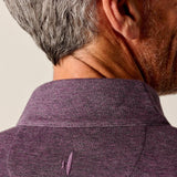 Close-up of a person wearing a purple shirt with a brand logo on a plain background