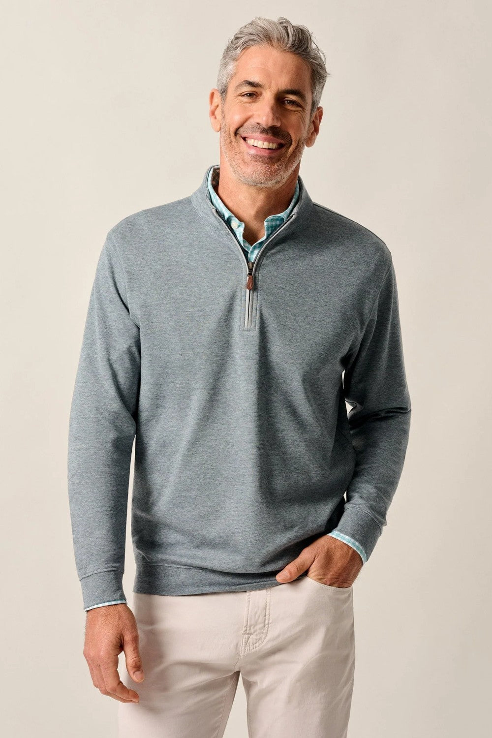Man wearing a gray quarter-zip sweater and light-colored pants against a plain background