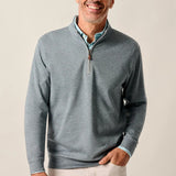Man wearing a gray quarter-zip sweater and light-colored pants against a plain background