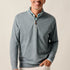 Man wearing a gray quarter-zip sweater and light-colored pants against a plain background