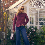 Woman in a burgundy jacket and blue jeans standing in front of a white gazebo.