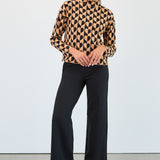 Woman wearing a heart patterned sweater and black pants against a white background
