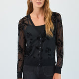 Woman wearing a black floral lace cardigan over a black top with blue jeans on a white background