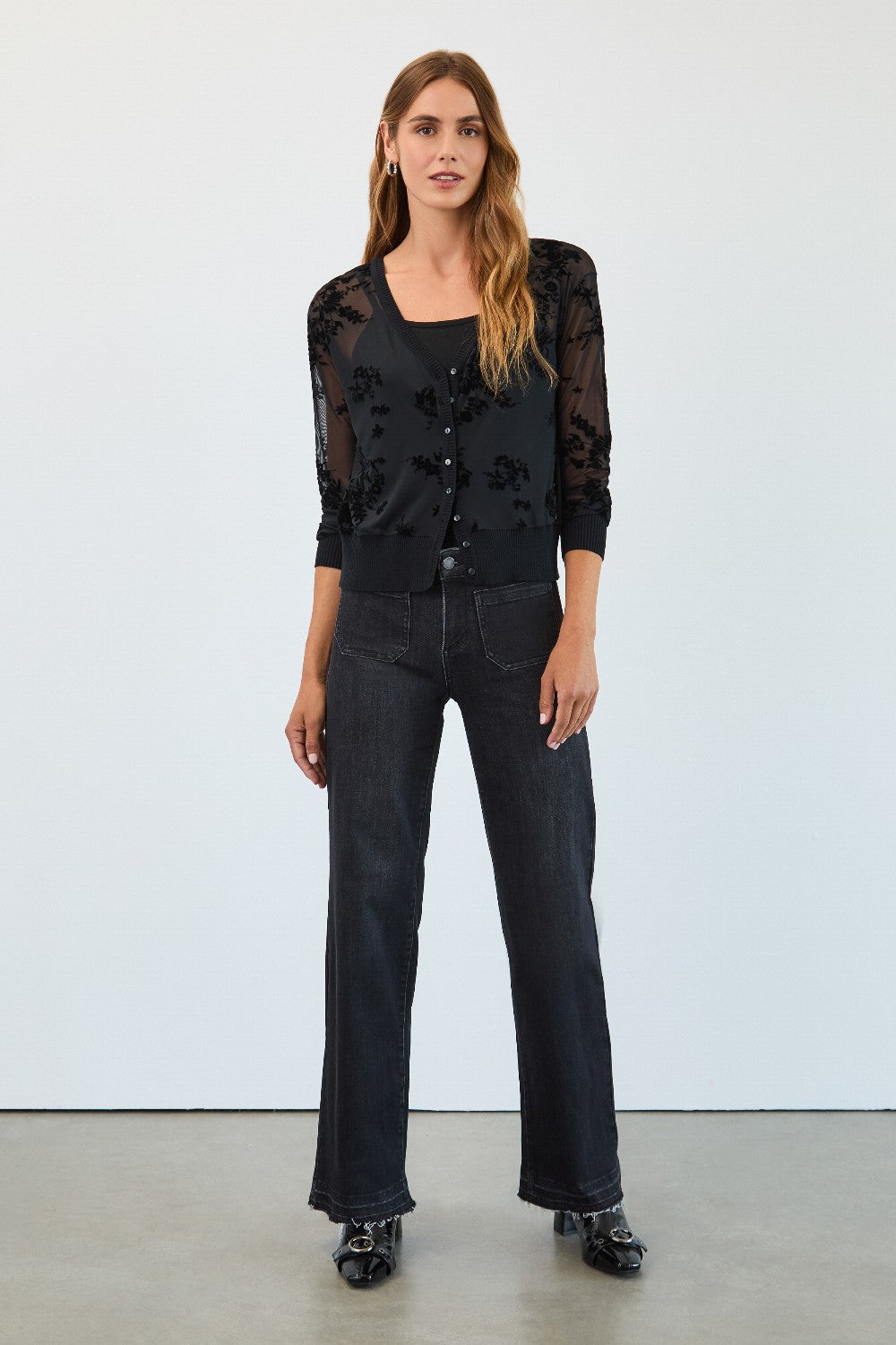 Woman wearing a black floral top and jeans against a white background