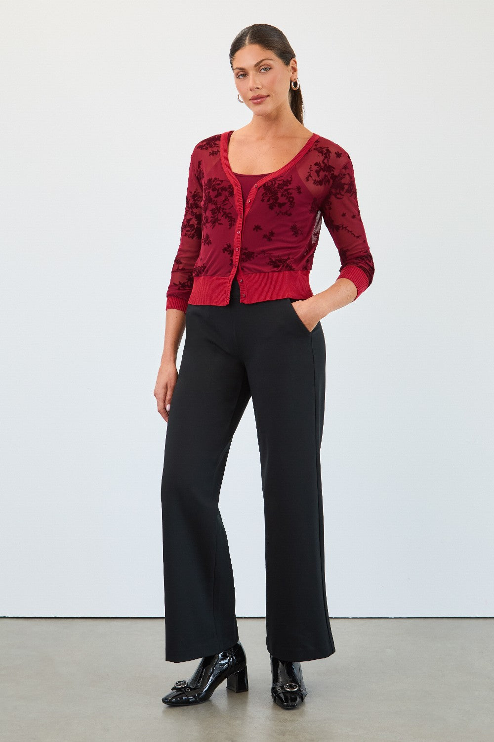 Woman wearing a red floral top and black pants against a white background