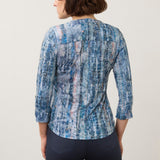 Woman wearing a printed blue top with blue pants on a light back ground.