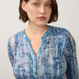 Woman wearing a printed blue top on a light back ground.