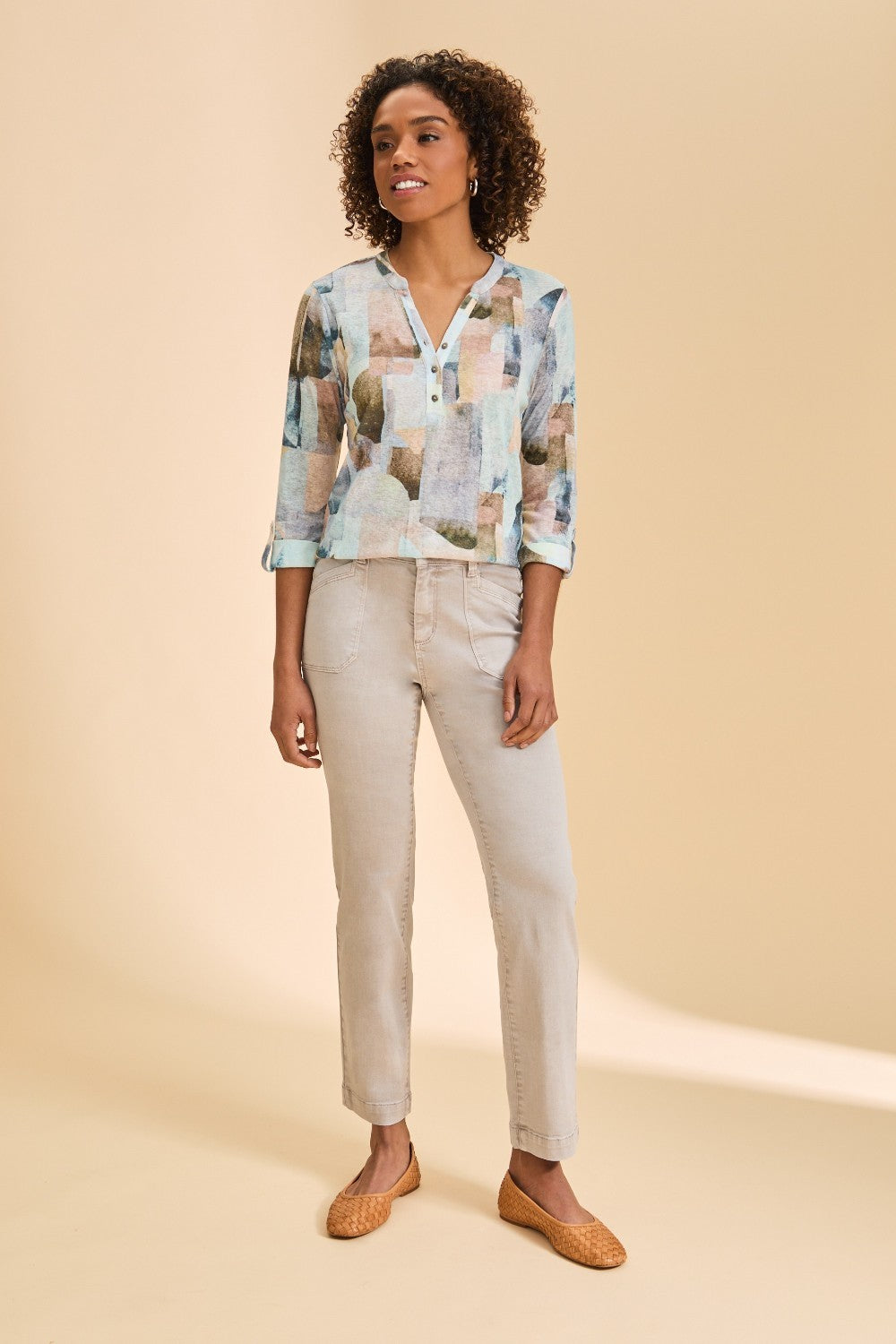 Woman wearing a patterned top and beige pants on a beige background