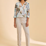 Woman wearing a patterned top and beige pants on a beige background