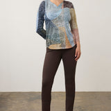 Woman wearing a printed top with brown pants and brown boots on a neutral background.