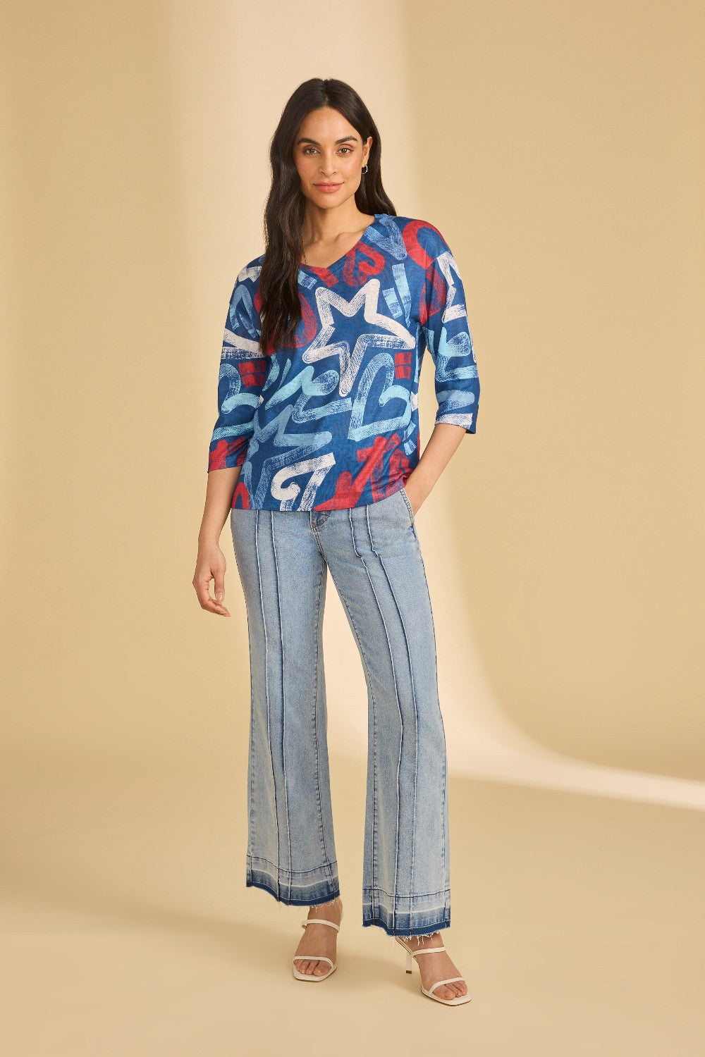 Woman wearing a blue patterned top and light blue pants on a beige background