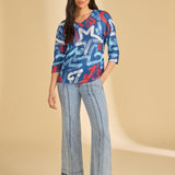 Woman wearing a blue patterned top and light blue pants on a beige background