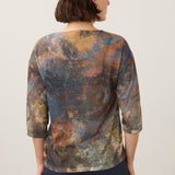 Woman wearing a printed top with coloured jeans on a light background.