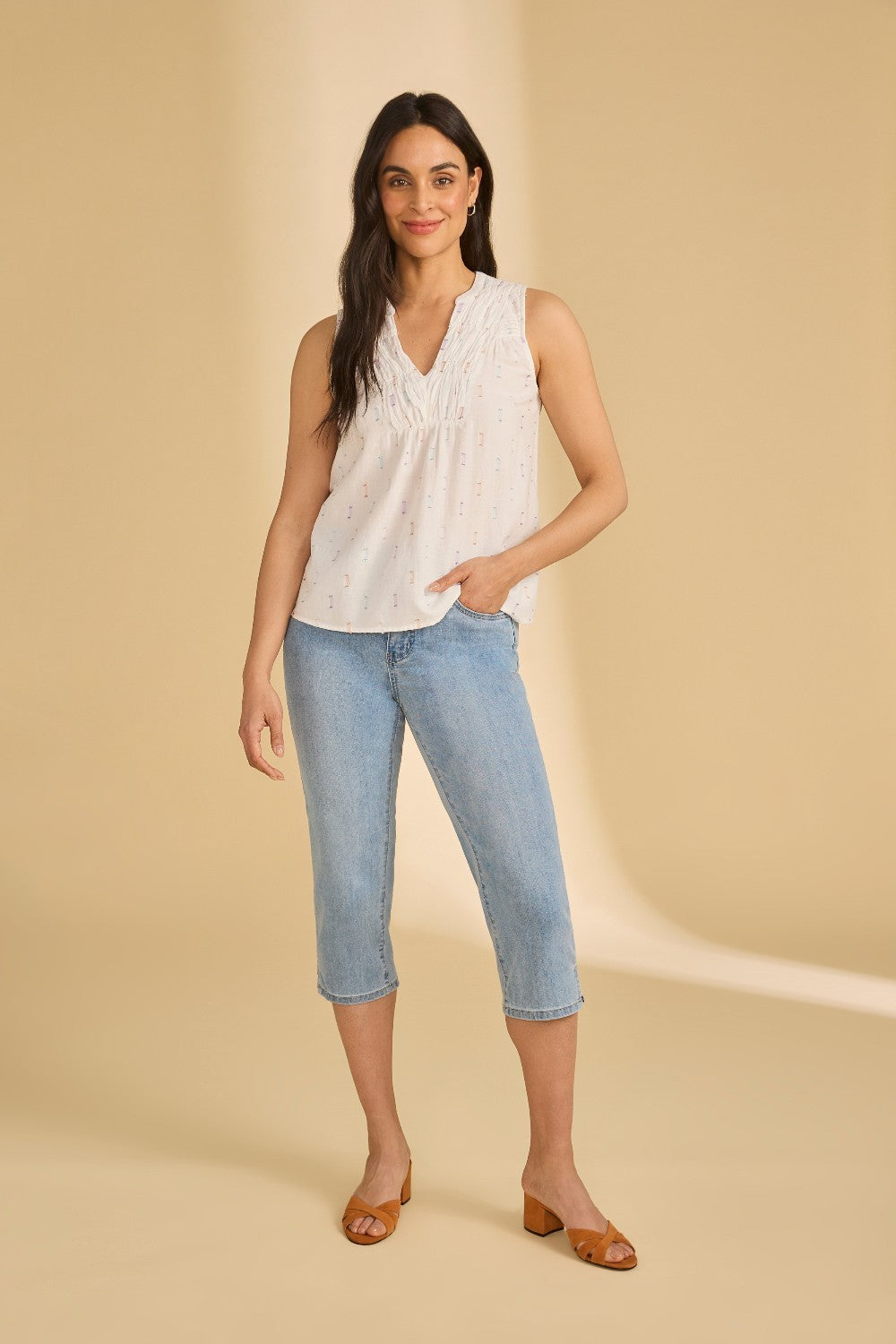 Woman wearing a white sleeveless top and blue jeans on a beige background