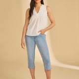 Woman wearing a white sleeveless top and blue jeans on a beige background