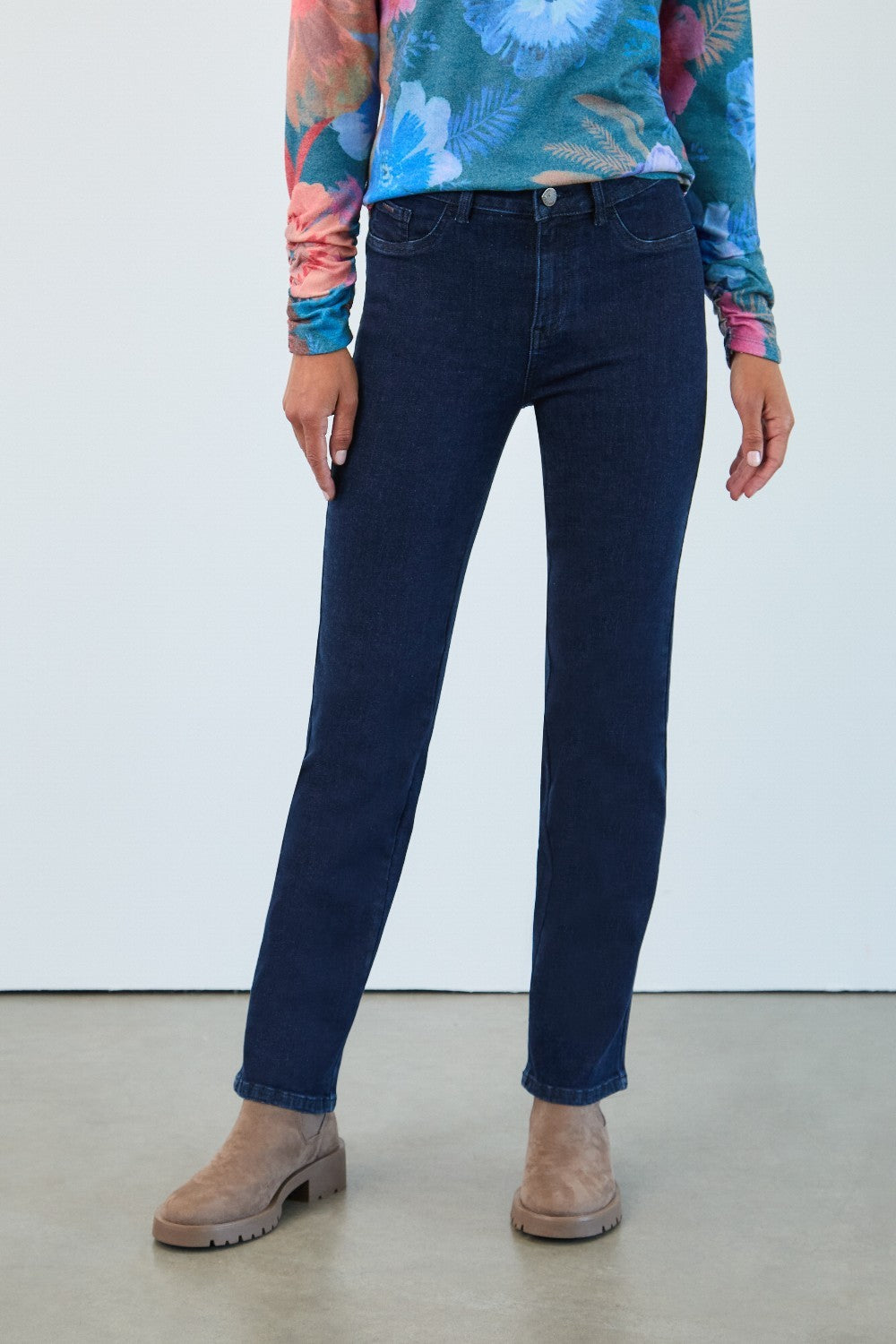Person wearing dark blue jeans and a colorful top against a white background