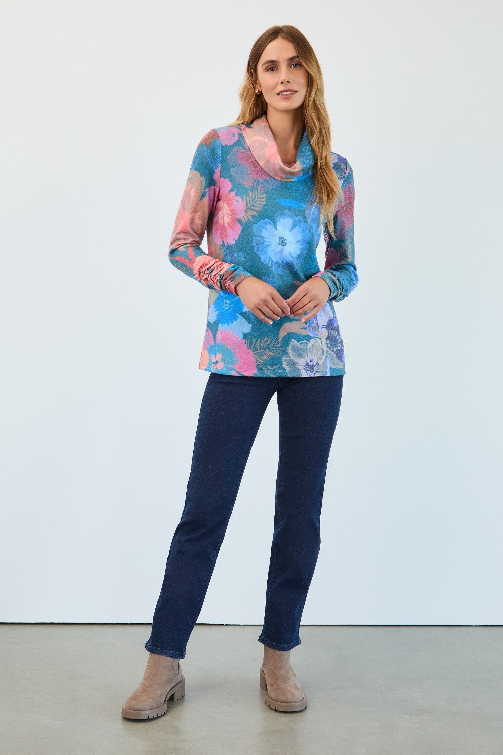 Woman wearing a colourful floral top and blue jeans against a white background