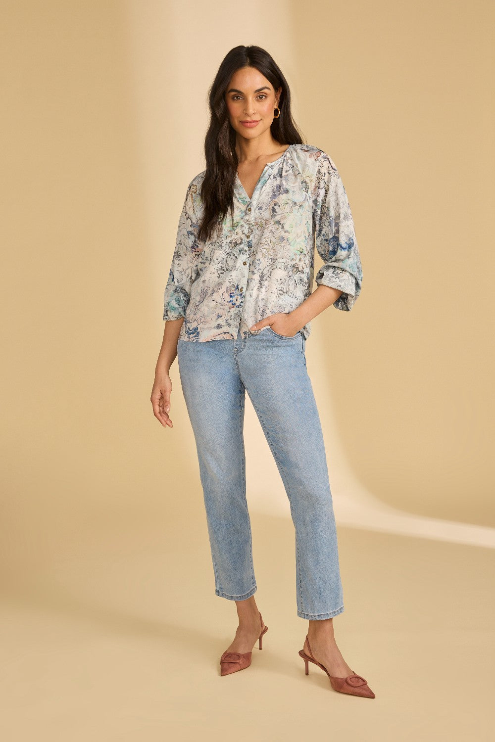 Woman wearing a floral blouse and jeans on a beige background