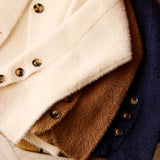 Three soft fuzzy button-front jackets stacked on a wooden surface, shown in cream, brown, and navy.