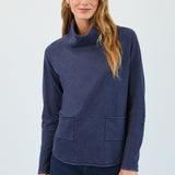 Woman wearing a navy blue cowl-neck sweater with pockets on a light gray background