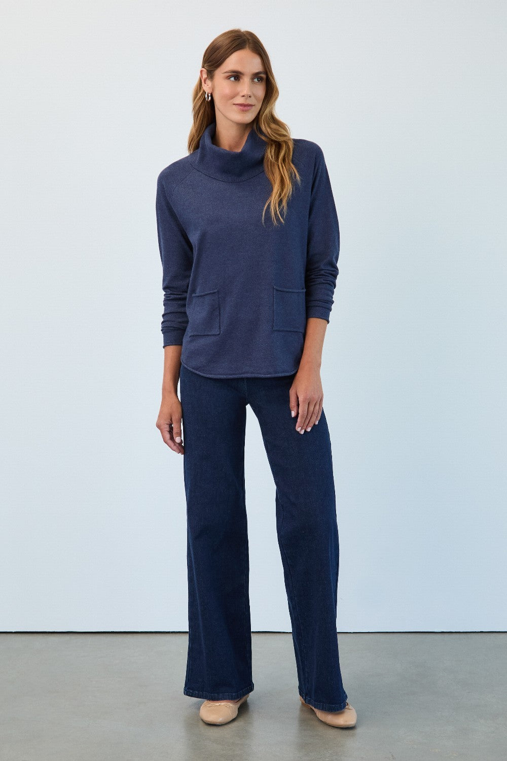 Woman wearing a navy blue outfit with a cowl neck top and wide-leg pants against a light gray background.