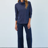 Woman wearing a navy blue outfit with a cowl neck top and wide-leg pants against a light gray background.