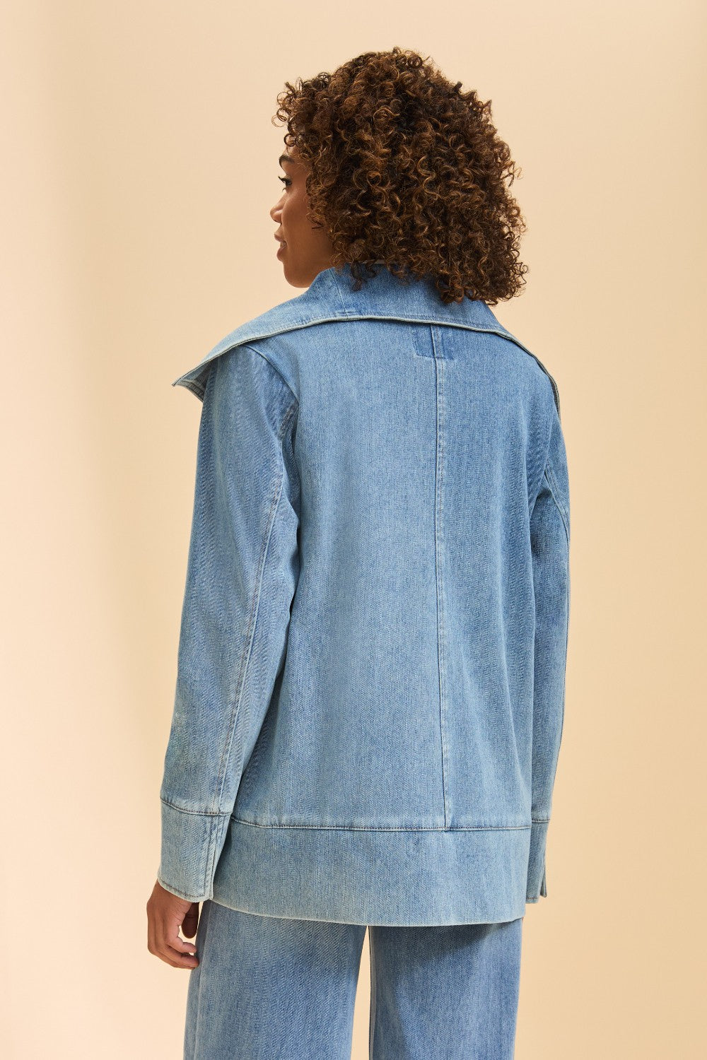 Person wearing a light blue denim jacket on a beige background