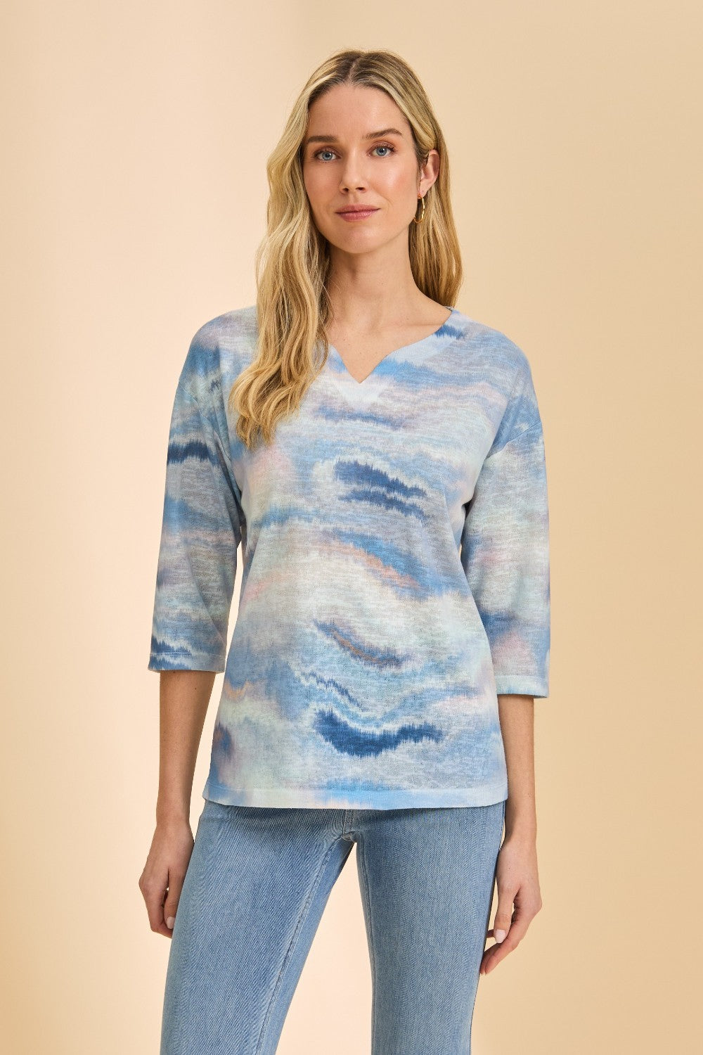 Woman wearing a blue patterned top and jeans on a beige background
