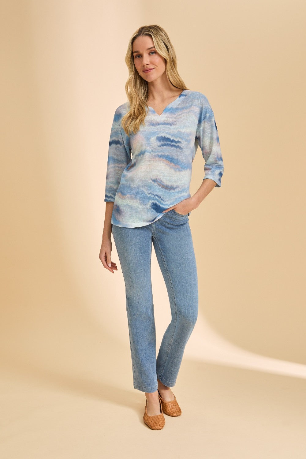 Woman wearing a blue patterned top and jeans on a beige background