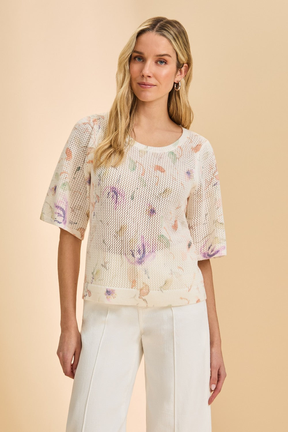 Woman wearing a floral top and white pants on a beige background