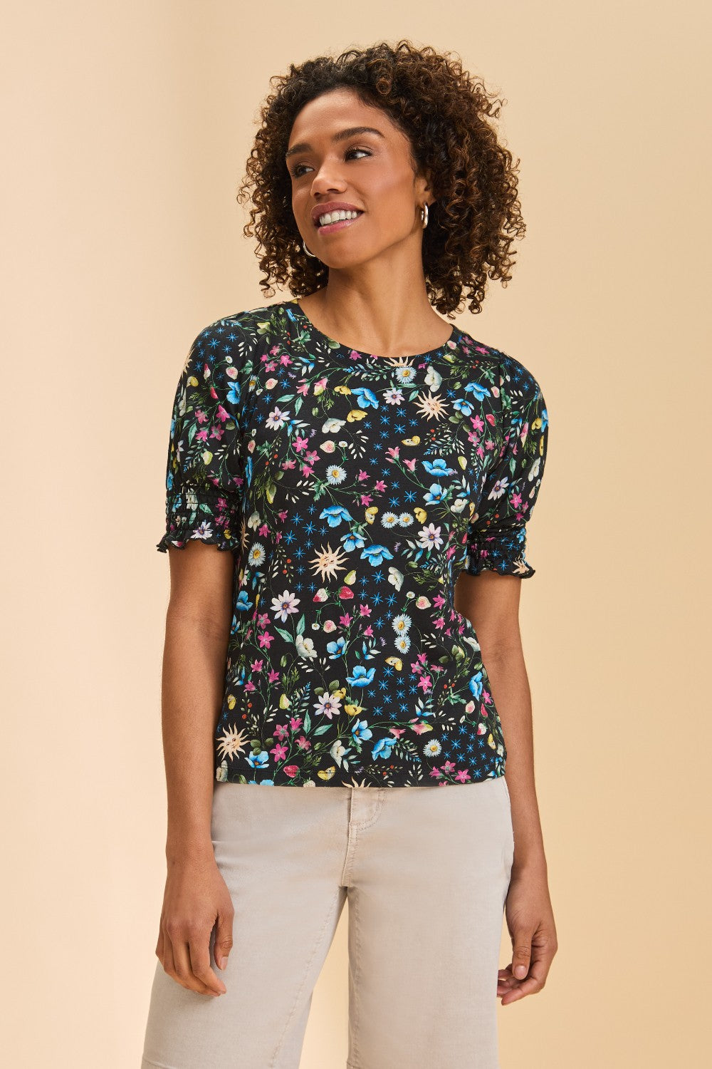 Person wearing multi coloured short sleeve printed top with light pant on a beige background