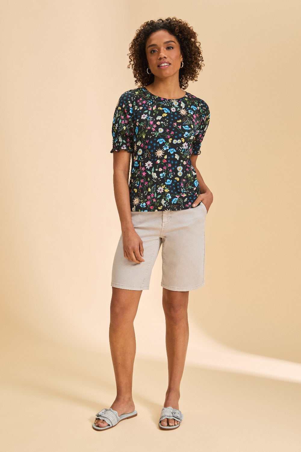 Person wearing multi coloured short sleeve printed top with light pant on a beige background