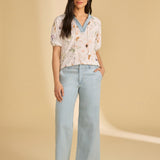 Woman wearing a floral top and light blue jeans against a beige background
