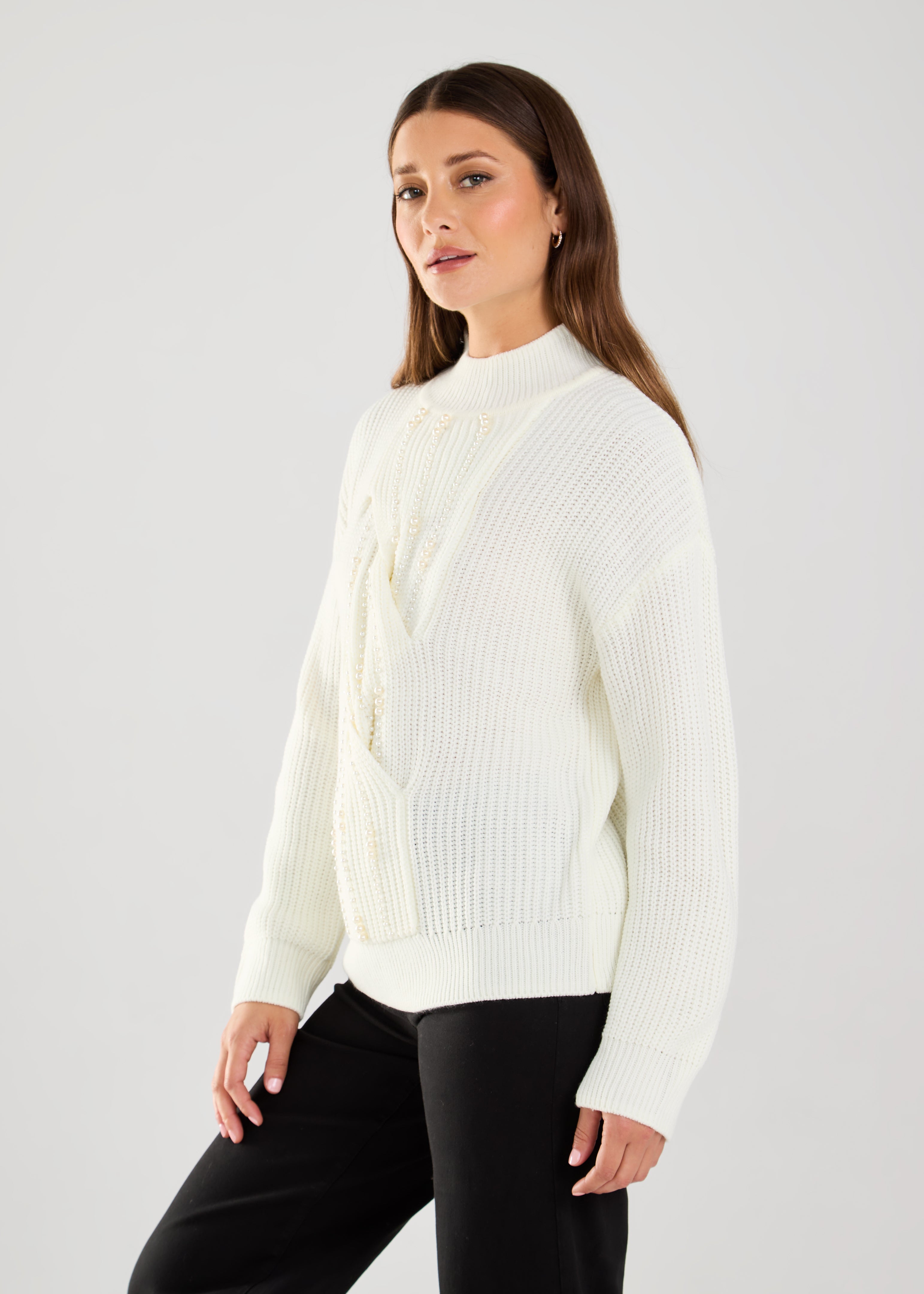 This cable knit sweater features delicate pearl embellishments, adding a touch of sophistication to a classic design.