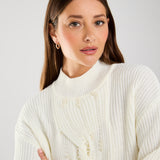 This cable knit sweater features delicate pearl embellishments, adding a touch of sophistication to a classic design.