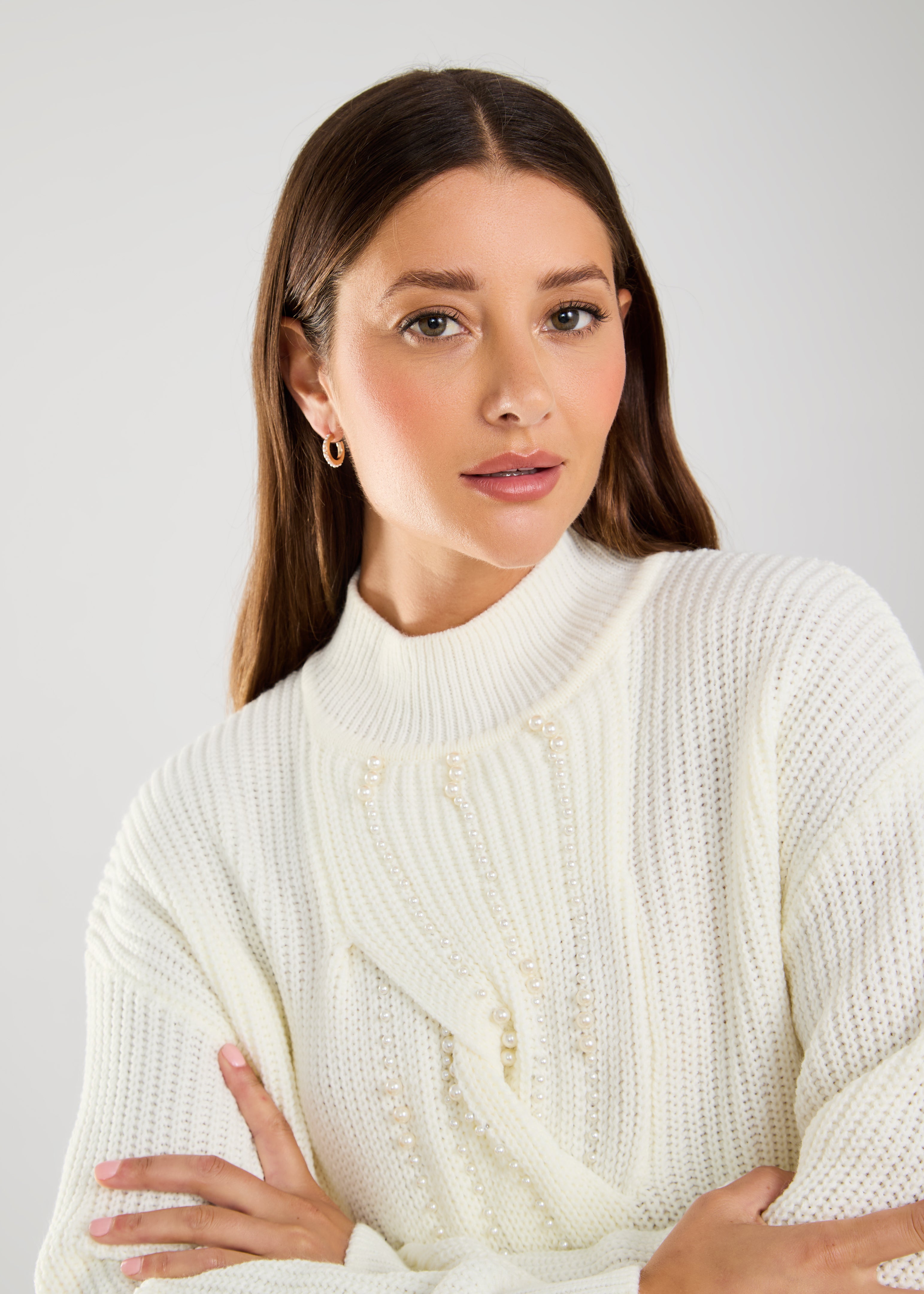 This cable knit sweater features delicate pearl embellishments, adding a touch of sophistication to a classic design.