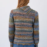 Person wearing a multicolored patterned sweater and blue jeans on a white background