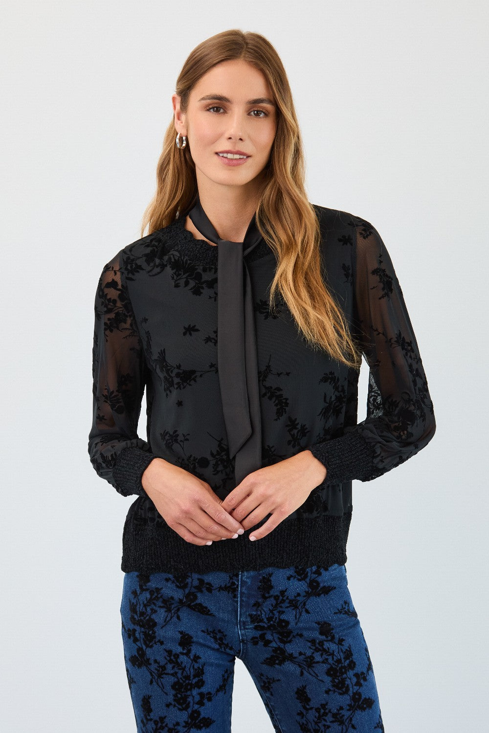 Woman wearing a black floral blouse with sheer sleeves against a white background