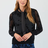 Woman wearing a black floral blouse with sheer sleeves against a white background