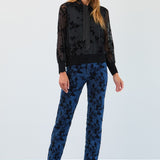 Woman wearing a black floral blouse and blue pants against a white background