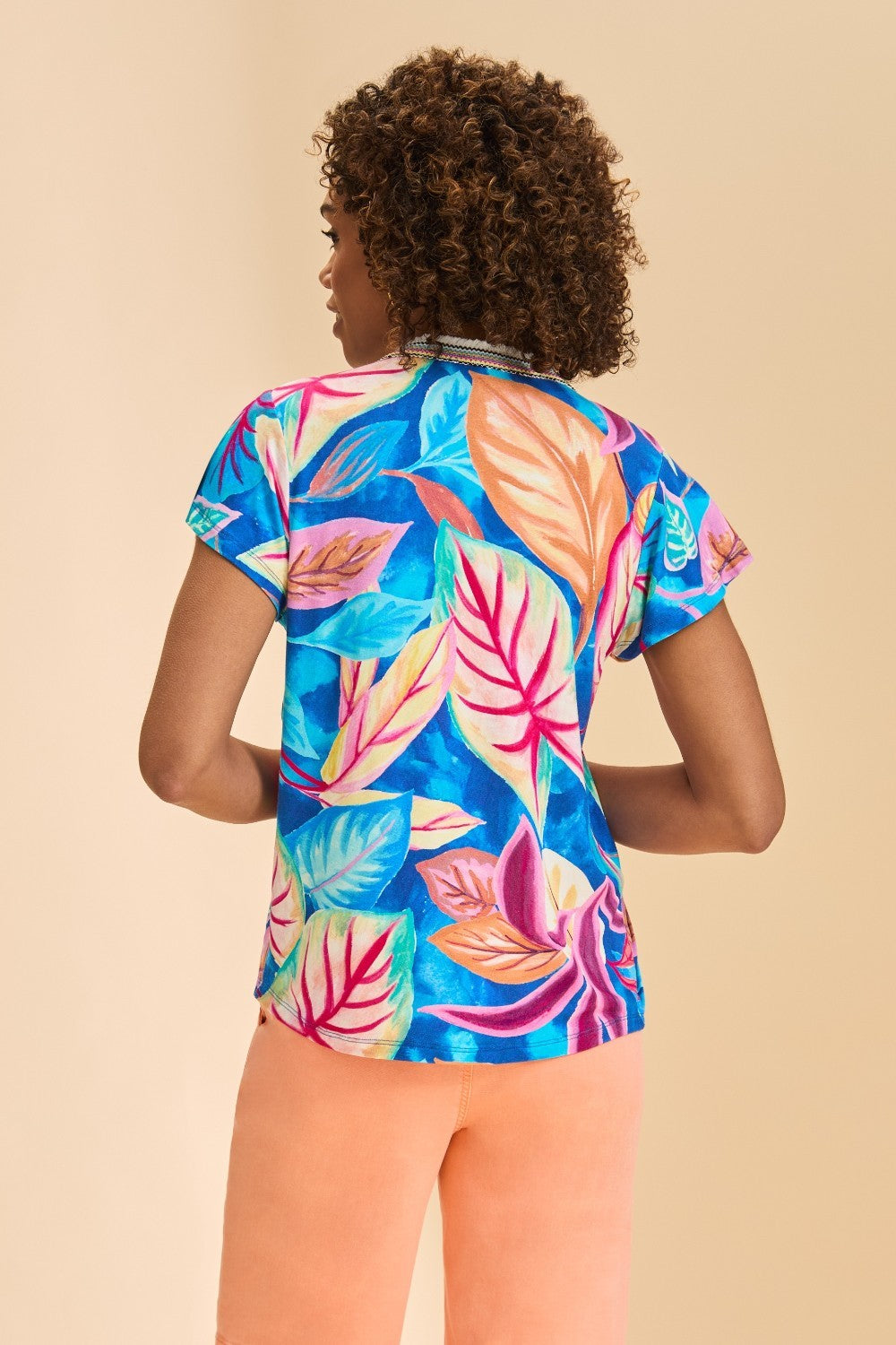 Woman wearing a colorful tropical print top and peach shorts on a beige background