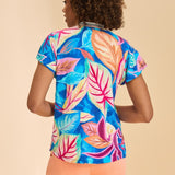 Woman wearing a colorful tropical print top and peach shorts on a beige background