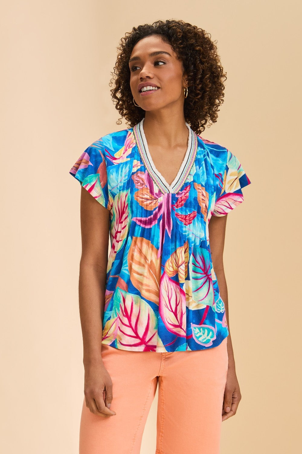 Woman wearing a colorful tropical leaf patterned top on a beige background