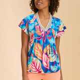 Woman wearing a colorful tropical leaf patterned top on a beige background