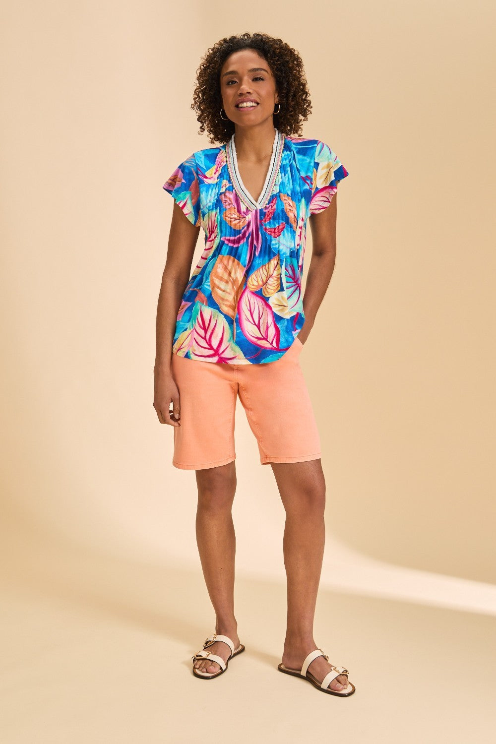 Woman wearing a colorful tropical print top and peach shorts on a beige background