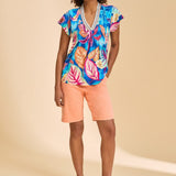 Woman wearing a colorful tropical print top and peach shorts on a beige background