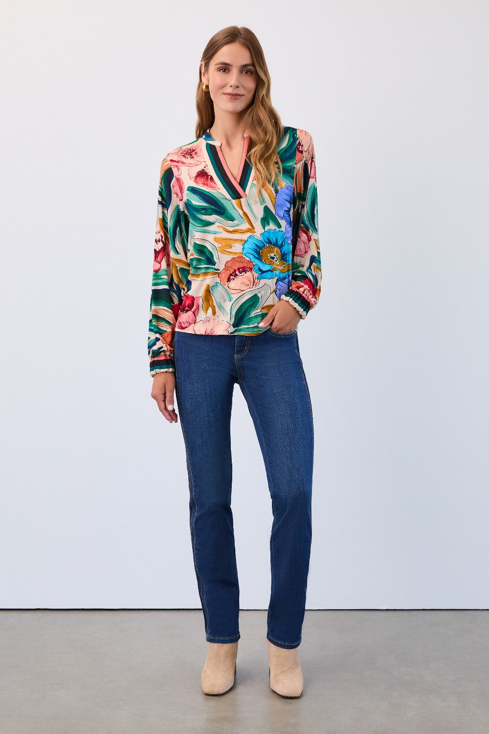 Woman wearing a colourful floral blouse and blue jeans against a white background