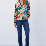 Woman wearing a colourful floral blouse and blue jeans against a white background