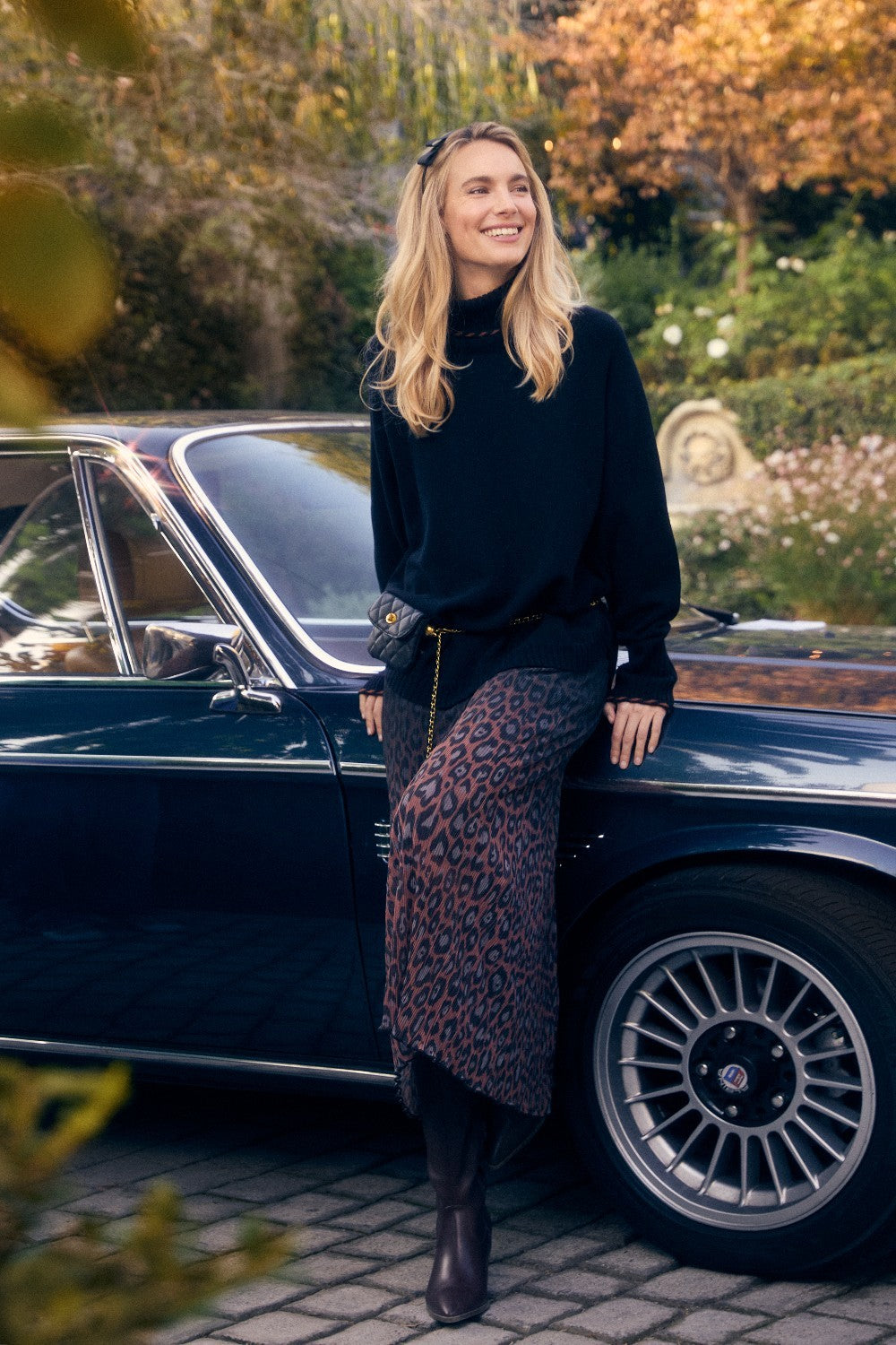 Woman standing next to a vintage car with autumn foliage in the background